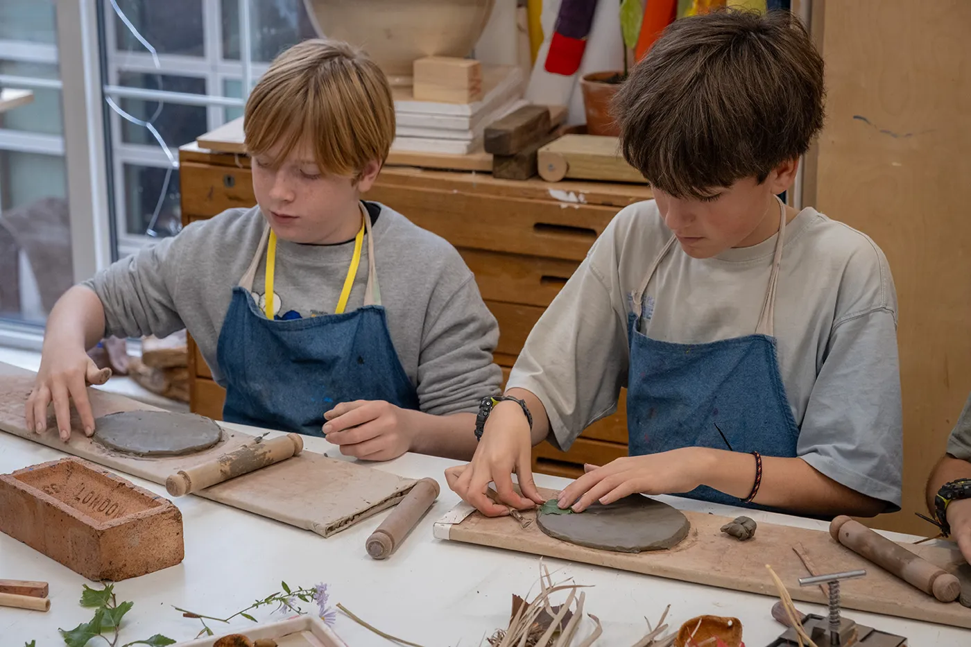 Two boys in aprons shaping clay at a workshop table