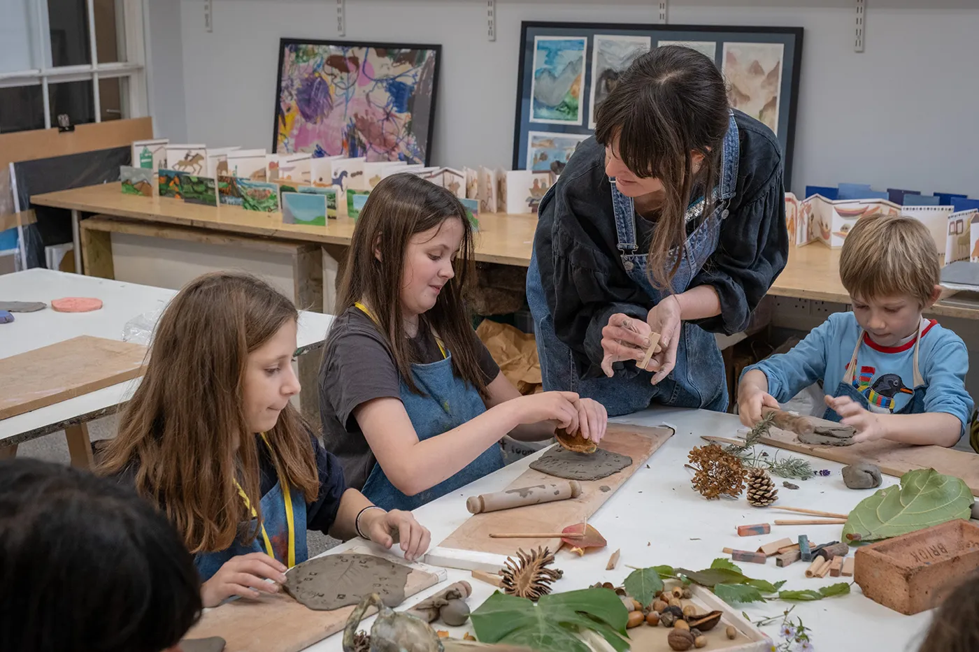 Children and an adult at a workshop table covered in clay, leaves and pine cones