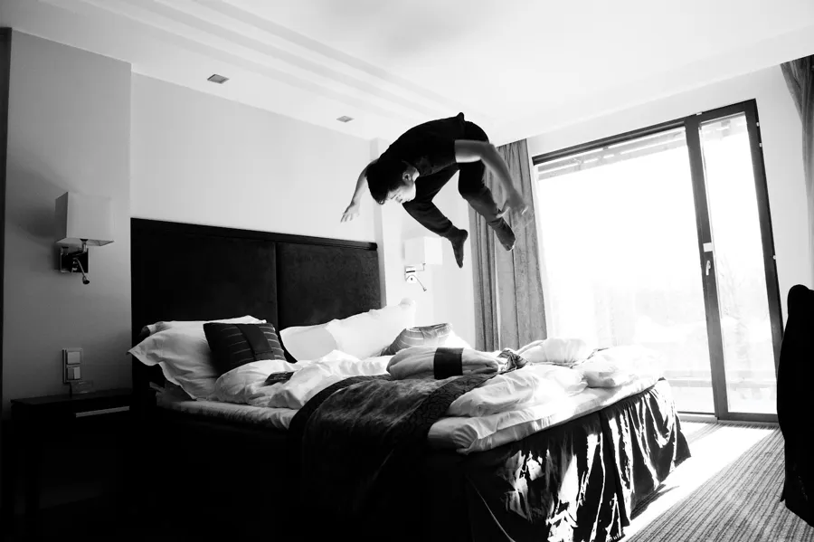 Black and white photograph of a figure leaping above a hotel bed