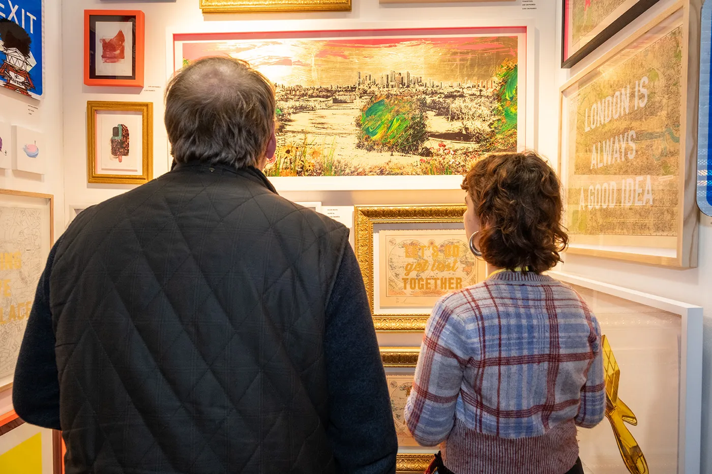 Two visitors looking at framed paintings of a city skyline