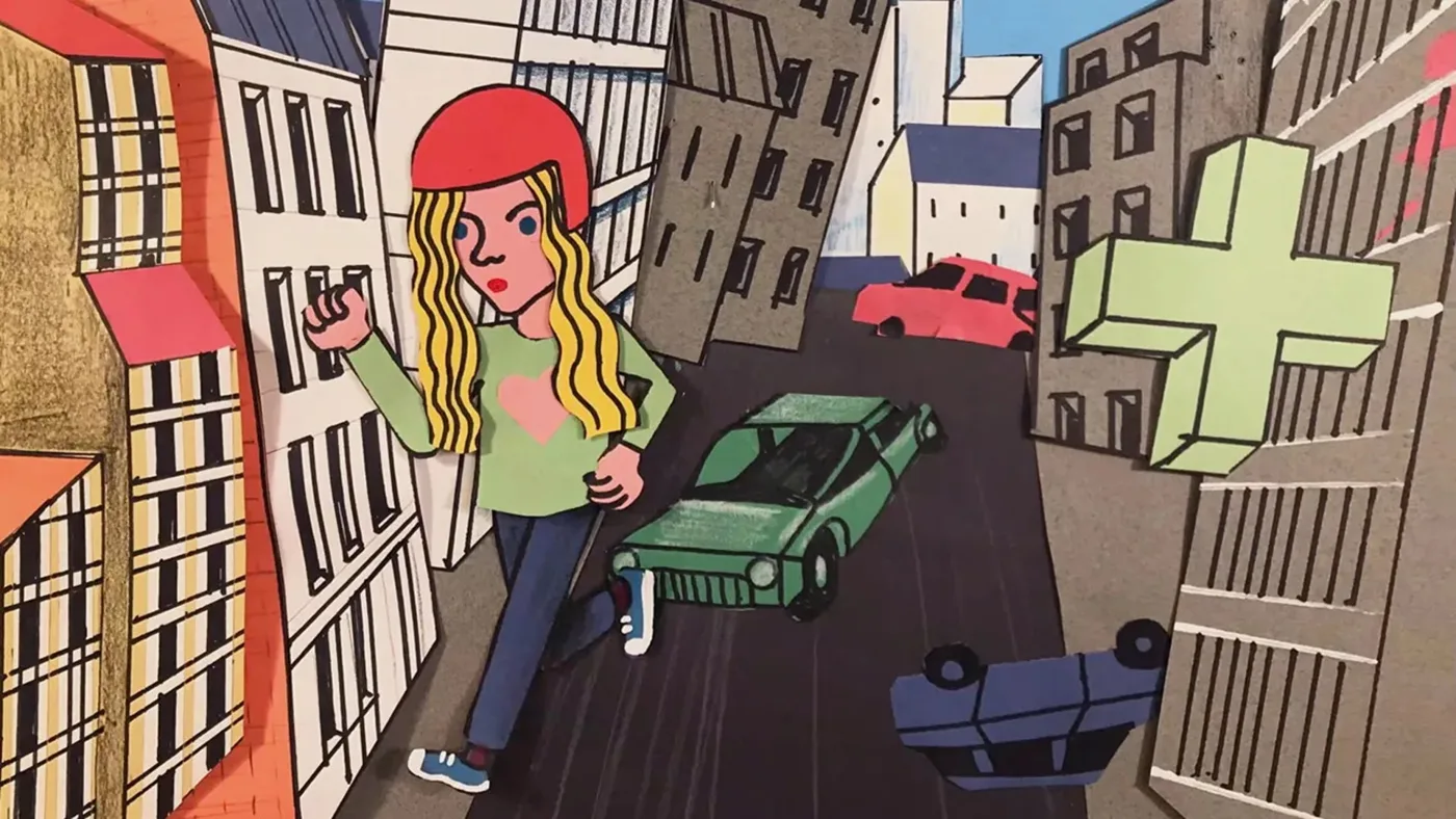 Paper-cut animation still of a girl in a red helmet walking down a street of drawn buildings with cars